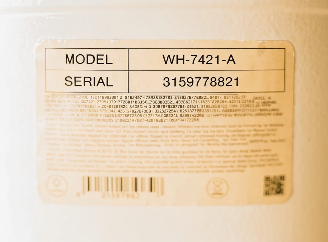 The stamped metal rating plate on a furnace in a basement, its model and serial numbers catching the light.